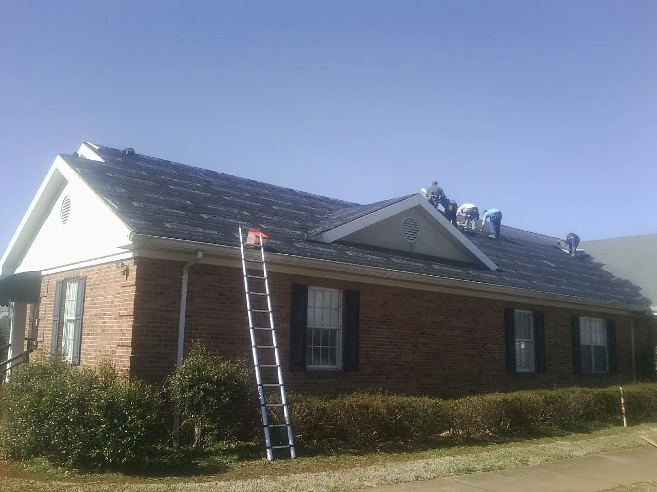 Crew tearing shingles off a brick ranch roof with a ladder set — Metal Roof Repair work by our crew in Valdese