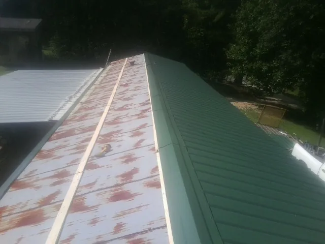 Old rusted panels beside newly installed green metal roofing — Wind Damage Roof Repair by Roofing Brothers in Valdese
