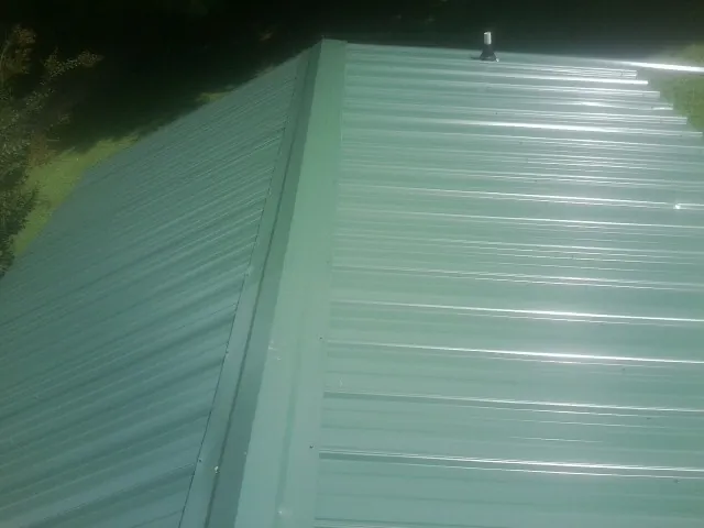 New green metal panels meeting at the ridge of a roof — Flat Roof Repair work by our crew in Valdese