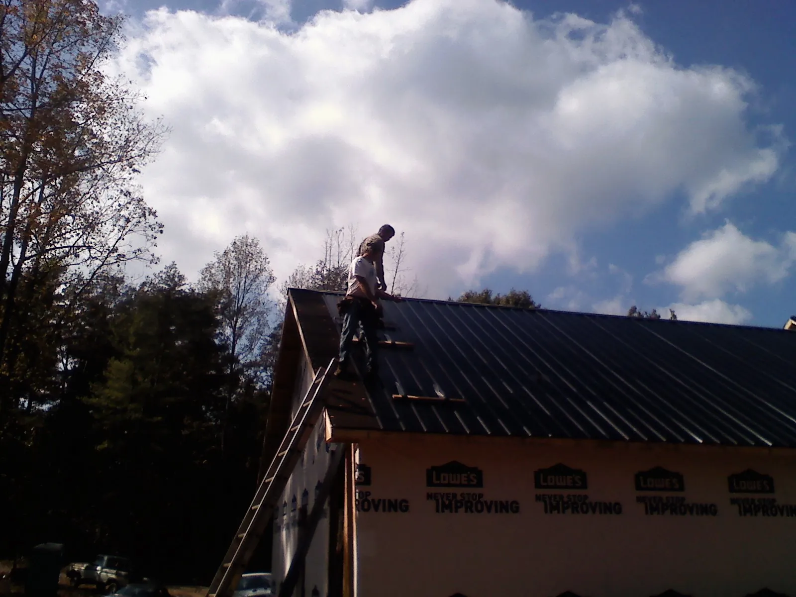 Roofer fastening dark metal panels high against a cloudy sky, from a Roof Inspection job in Valdese