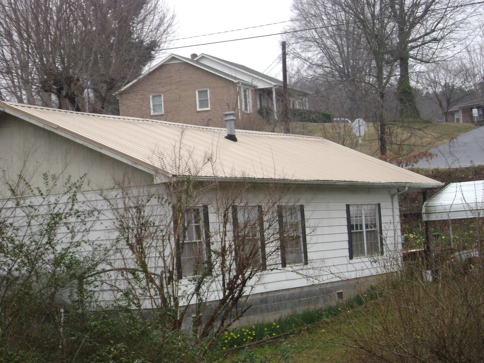 Tan metal roof on a white sided house set into a hillside — Commercial Roofing by Roofing Brothers in Valdese