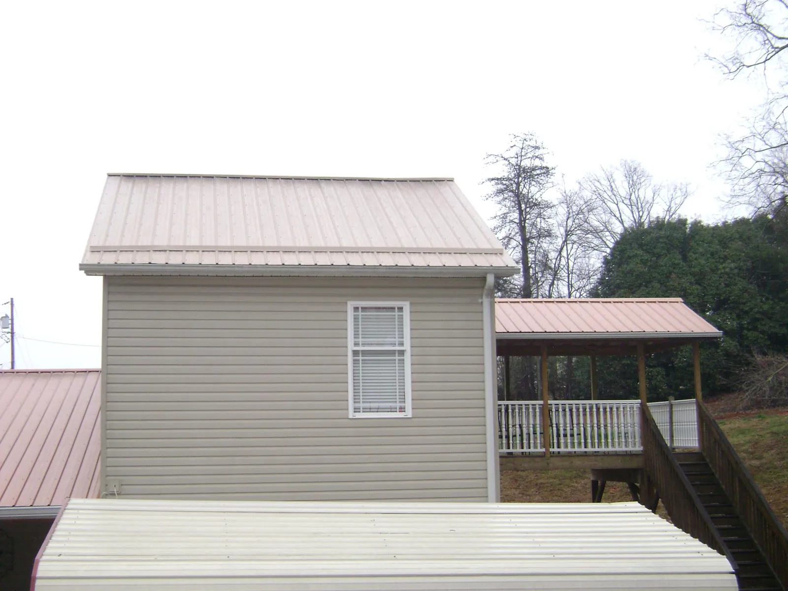 Tan metal roofs on a two story addition and attached porch, from a Roof Replacement job in Valdese